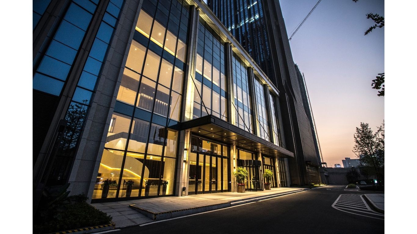 Modern glass building entrance with illuminated interior and evening sky in the background.